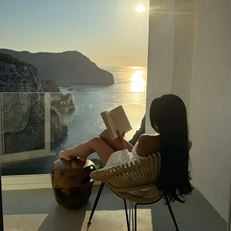 Mulher a ler com vista para o oceano ao pôr-do-sol